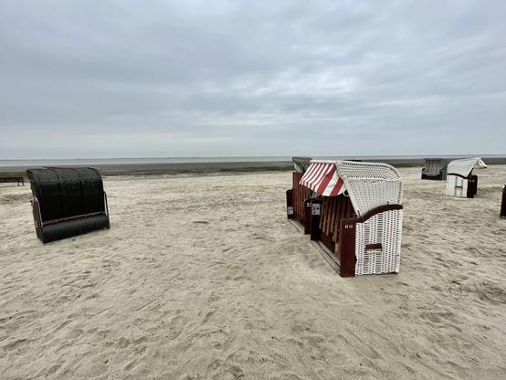 Blick auf Strandkörbe im Sand,  dahinter das Meer, grauer Himmel
