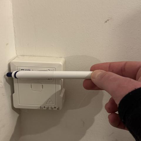 Glasfaser-Dose für FTTH an der Wand, die ID wird mit einem gehaltenen Kugelschreiber verdeckt.