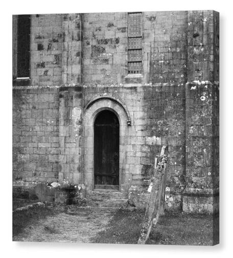 Vintage looking black and white film photograph showing a small narrow door at the back of an old church.  The image is shown printed upon a square box canvas.