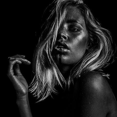Porträt einer Frau mit schulterlangem Haar, dramatisch beleuchtet, mit Schatten auf dem Gesicht und erhobener Hand