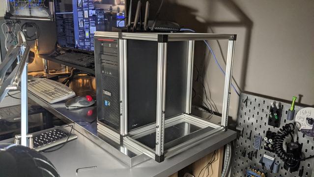 a desktop computer surrounded by a metal frame. a bunch of networking equipment is balanced on top of the computer instead of being nicely mounted in the rack.