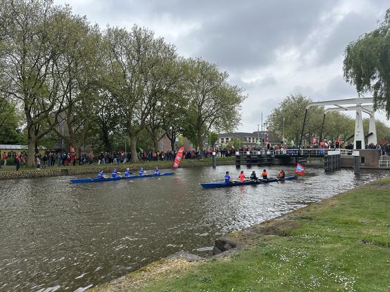 Rowers join the crowd of protesters marching along a canal and in a bridge. Rowers and marchers are carrying red flags.