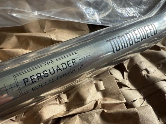 Central section of polished alloy bicycle handlebars with etching reading 'the persuader, built to explore' and 'tumbleweed'.