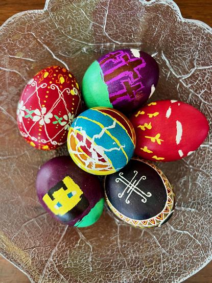 A variety of painted easter eggs in a glass bowl from an overhead view. One is obviously a Minecraft inspired creation.