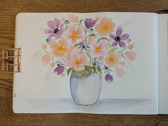 This is a watercolor painting of flowers in a vase. The flowers are peachy pink, peach, pinky purple, and bluish purple with some yellowish green leaves and greenery. Some of the flowers are open others are buds. Some of the floral centers are a warm yellow some are dark blue.