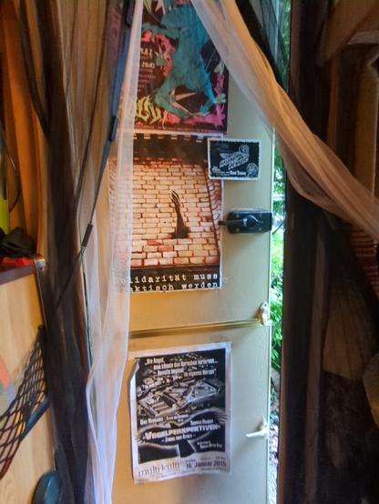 Door of a caravan that is slightly open. There are several posters on the door.