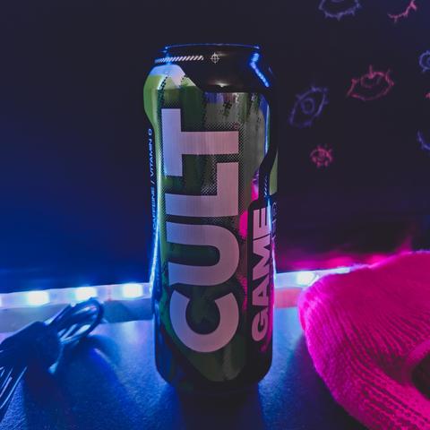 can of cult game changer, green with black, placed on a black table, backlit with white leds strip. Black wall behind has a bunch of pink and blue eyes drawn on it. On the table there's a hot pink balaclava, and a bunch of wires. image by wannabekingpin aka vakaris.