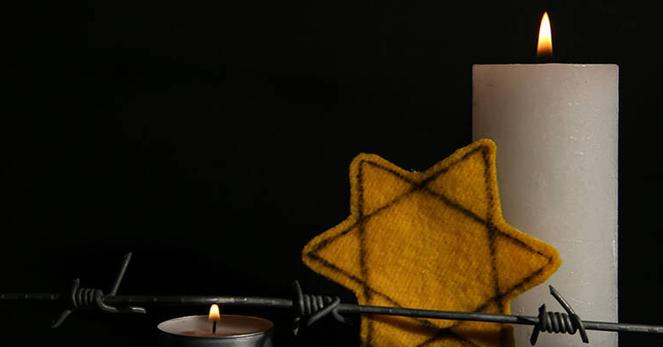 image features two lit candles—one large and one small—set against a dark background, with a yellow Star of David patch and a strand of barbed wire in the foreground. The elements evoke memory, mourning, and resilience, symbolizing the Holocaust and the suffering of the Jewish people.