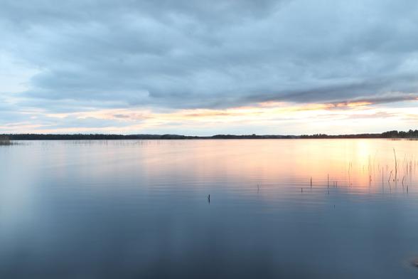 The sun illuminating a dense cloud cover from behind, reflecting in the surface of a lake glossy from time exposure