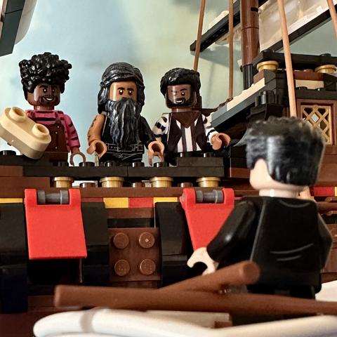 A scene from Our Flag Means Death in Lego. Roach, Ed, and Ivan stand on the side of the Revenge looking down at Izzy, whose back is to the camera. He is standing in a dinghy. Roach is holding a sandwich.