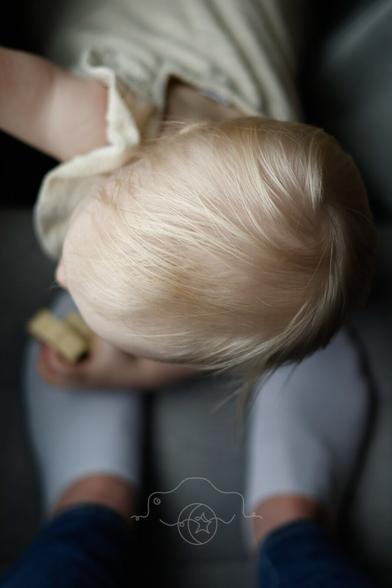 A view of a toddler playing with a toy at her parent's feet in the light of a window on a cloudy day.