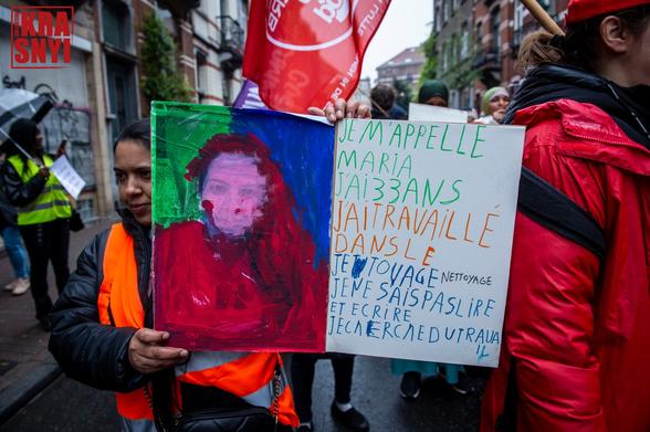 Une dame porte un panneau "JE M'APPELLE MARIA, J'AI 33 ANS, J'AI TRAVAILLÉ DANS LE TATOUAGE, NETTOYAGE, JE NE SAIS PAS LIRE, PAS ÉCRIRE, JE CHERCHE DU TRAVAIL"