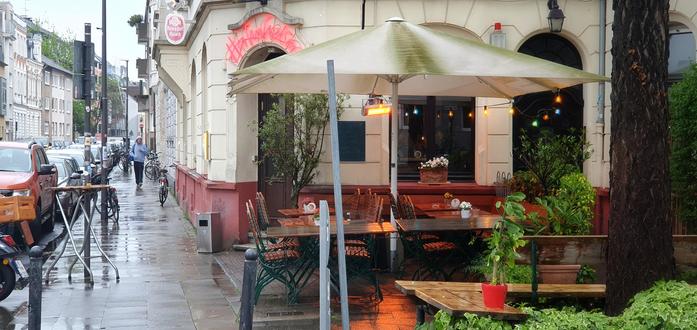 a restaurant at a street corner in the rain, with outside seating under a parasol
