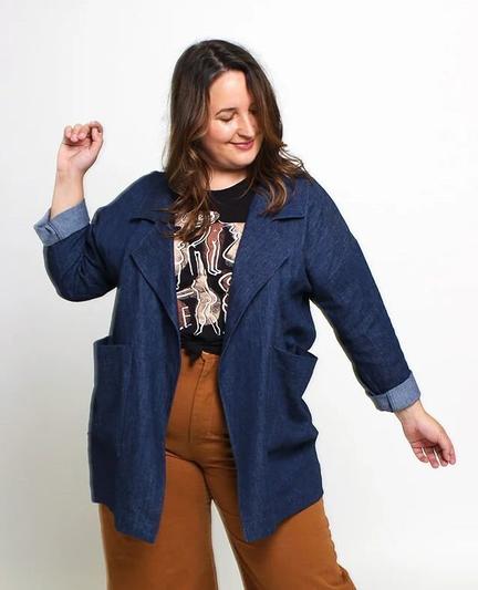 Caroline wears a thigh-length denim jacket with wide lapels, a graphic tee, and brown pants.