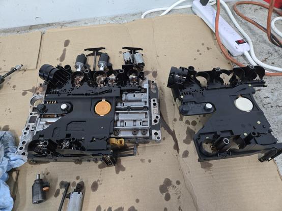 A picture of a transmission valve body with a new conductor plate sitting beside it. It's sitting on brown cardboard.