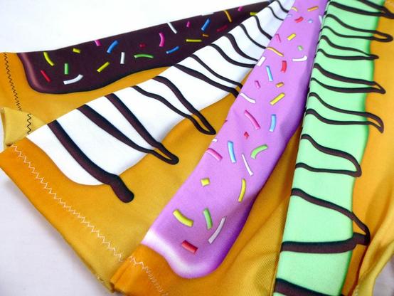 four handmade sleeves with donut designs: one with chocolate icing and rainbow sprinkles, one with white icing and a chocolate drizzle, one with strawberry icing and pastel sprinkles, and one with mint icing and a chocolate drizzle