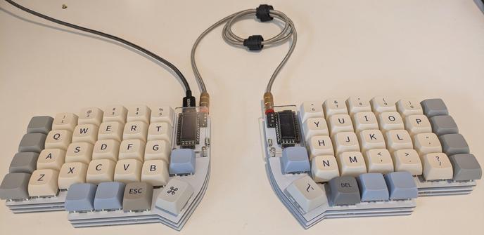 Ergonomic split keyboard with beige, blue and gray keycaps. Model type is called a lily58.