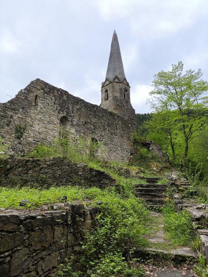 Eine alte Kirchen Ruine auf dunklem Stein, die von Gras umwachsen ist.