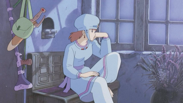 Nausicaä from the film Nausicaä of the Valley of the Wind. She is wearing a light blue tunic with a scooped neckline that comes to her knees. There is lilac trim around the neckline and hemline, plus a sash around the waist in the same color. She wears a light blue beaded hat and off-white trousers as well. She is seated by a window lit by moonlight and looks out with a knee tucked up.