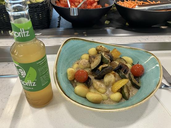 Gnocchi with some sauce and vegetables in a bowl, and a drink