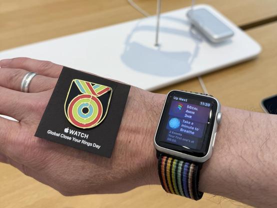 A physical pin replicating the Global Close Your Rings award next to a 10 year old Apple Watch