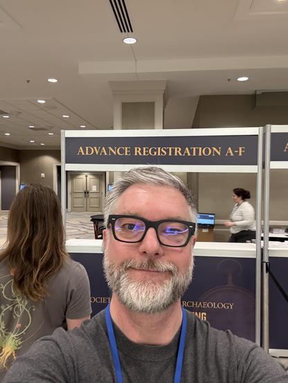 A bearded man standing in front of a kiosk with a sign reading “Advanced Registration A-F”
