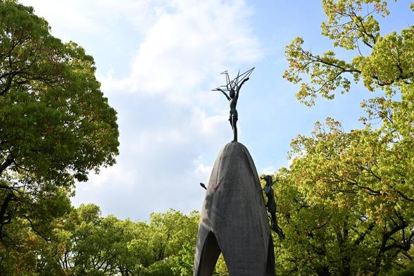 The children's memorial. A sculpture of a child holds the shape of an origami crane aloft. It is surrounded by greenery and blue skies.