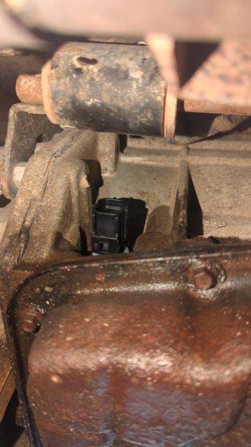 A far view of the line pressure sensor on a 545RFE automatic transmission. It's just barely visible sticking out of the side of the transmission between the housing and the exhaust.