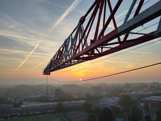 lever de soleil avec de la brume et des traces d'avion dans le ciel, avec une flèche de grue en travers et un petit point c le soleil rouge