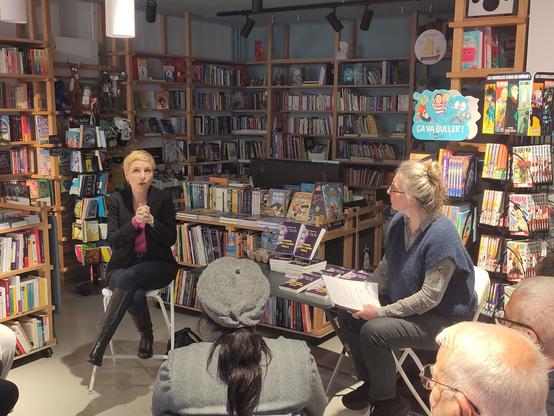 deux femmes assises dans une librairie. à gauche, Clémentine Autain est visiblement en train de parler. dans le fond , des rayonnages de livres.