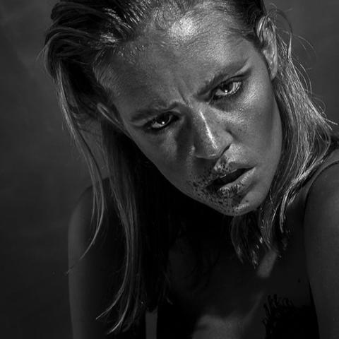 Frau mit nassem Haar und intensivem Blick, Gesicht und Lippen mit dunklem Material bedeckt