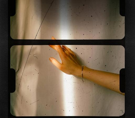 Hand mit Armband, die gegen eine helle Wand mit Schatten und Staubpartikeln streicht