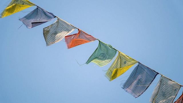 Drapeaux de prières tibétains multicolores flottant dans le vent sous un ciel bleu clair, suspendus en ligne au monastère de Thrangu Tashi Yangtse. Les drapeaux, ornés de textes sacrés, symbolisent la paix, la compassion, la force et la sagesse.