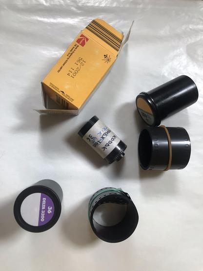 Color photograph of film roles, film canisters and packaging, including:
* Kodak Tri-X package with expiry date 12/2001
* Kodak Tri-X and Ilford Delta 3200 canisters
* a self-role spool originally labeled T-MAX 100 but overwritten with Tri-X