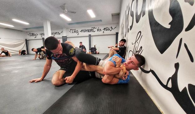 Se ven dos luchadores haciendo grappling. Uno está intentando hacer una llave de pie y el otro la está defendiendo