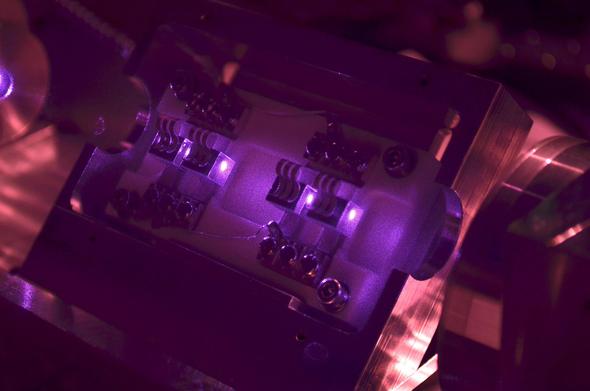 Das Licht des kürzlich bei GEO600 installierten neuen Lasersystems (in violett erkennbar) strahlt durch vier Würfel aus einem speziellen Kristallmaterial, die in einem weitgehend abgedunkelten Bereich in einer komplizierten Halterung aus Metallteilen sitzen.