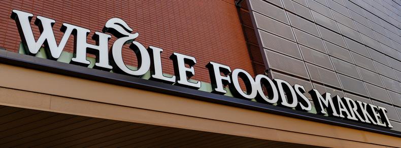 The words "WHOLE FOODS MARKET", the on-building signage for one of those stores, stretch from the upper left to lower right of the frame, which is in a wide 65:24 aspect ratio.