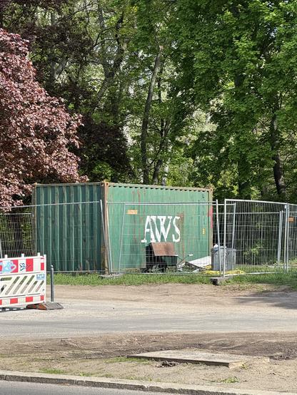 A rusty metal construction site container with the letters "AWS" printed on the side. It's standing on the side of a road in front of trees