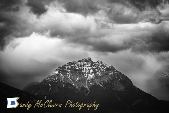 Pyramid style mountain with snow remnants at the top under a looming overcast sky.