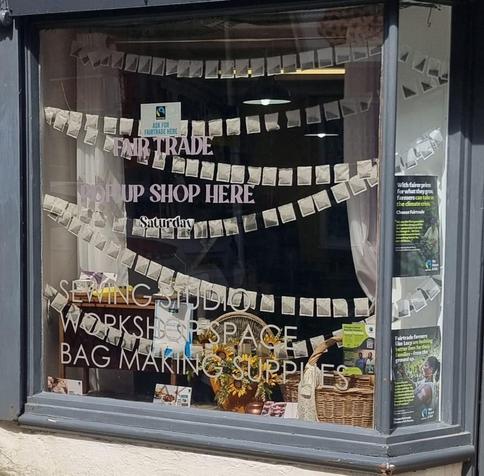A shop window decorated with hunting made out of tea bags, Fair Trade products, and posters. Text reads "Fair Trade pop up shop here Saturday"