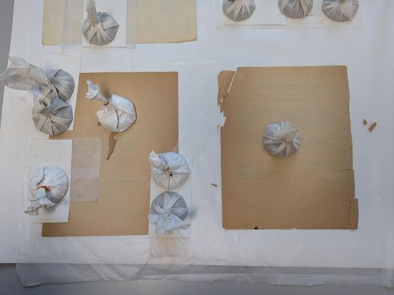 Two pieces of beige brown paper. Pieces creased and broken off at corners. Partial repairs under pieces of blotter held down with weights.
