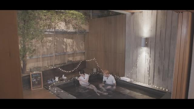 Hyunjin and Bang Chan sitting in a large bath. It seems to be night time. There are fairy lights draped around them.