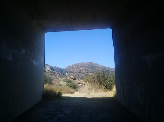 a square window view of a scrubland mountain scene from inside a large metal storm drain