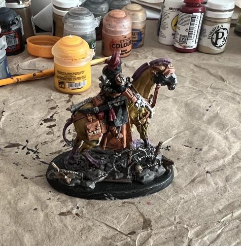 Warhammer 40K Miniature

Krieg Lord Marshall. Black uniform with orange gloves and boots, riding horse like creature with yellow fur and purple mane. Red hair coming out of top of helmet. 

Facing right, drawn pistol visible.
