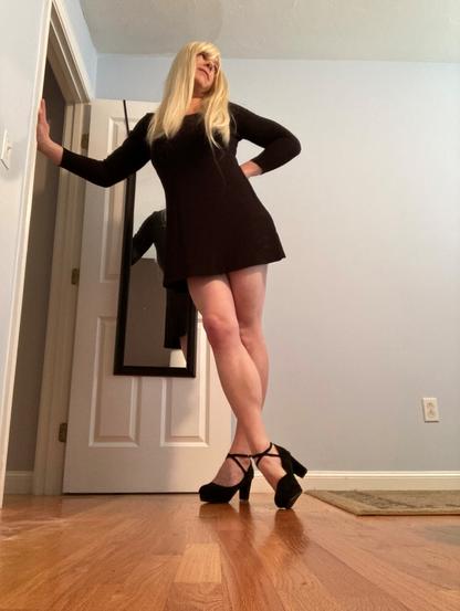 blonde woman with thigh length black dress and black strap high heels.
