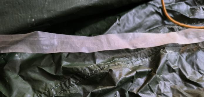 A part of a green flysheet. A white strip which is the seal has detached from the seam itself.
