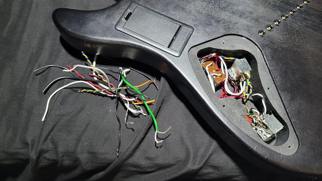 Zoomed out detail of the same control cavity from the previous image. This picture features a pile of colored wires next to the guitar body. These wires were part of the stock wiring job and were all trimmed as the length was unnecessary and created a "rats nest" in the cavity. A 9 volt battery door can be seen to the left of the control cavity.