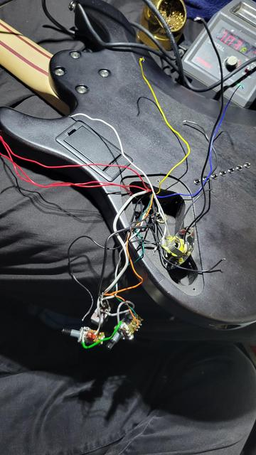 Image of the same control cavity before rewiring. All of the controls and wires have been pulled out of the guitar and are strewn everywhere. Lots of long, colored wires are seen connecting the electronics together. All of this mess used to be stuffed inside the small cavity. A soldering iron set to 703 degrees F can be seen in the top right of the image. Next to it is a brass sponge for cleaning the iron tip.