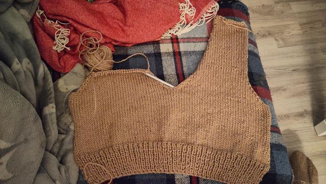 Light brown knit vest front piece laid on a sofa. One shoulder is finished and the other is still being worked on.
