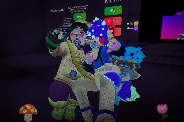 The photo shows two furry characters in a virtual environment. One is wearing a cream-colored hoodie and purple pants, while the other is in a diaper and blue outfit. They appear to be interacting, possibly dancing or playing a game, in front of a screen showing a video mirror feature.